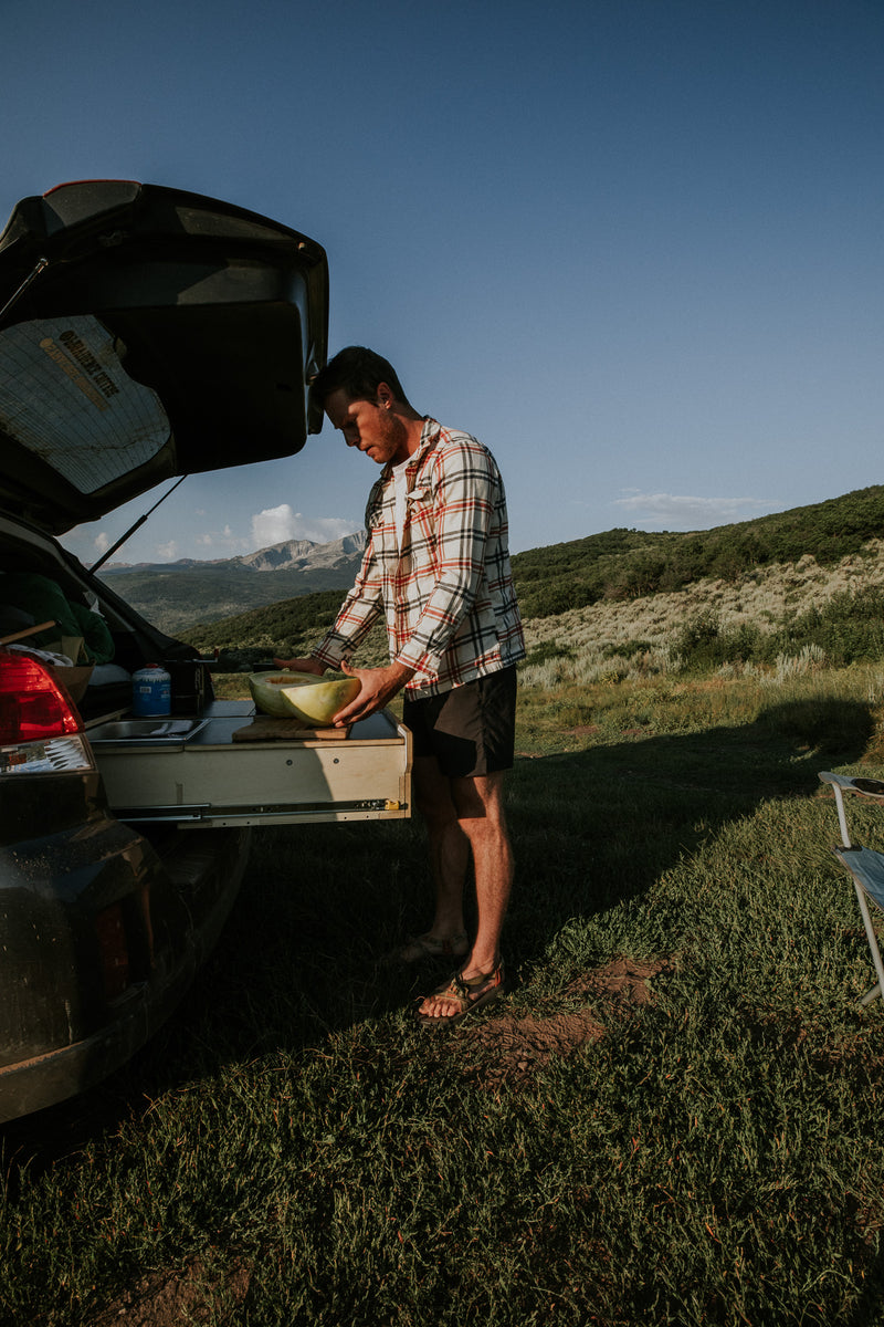 Person preparing food from a car trunk in a scenic outdoor setting